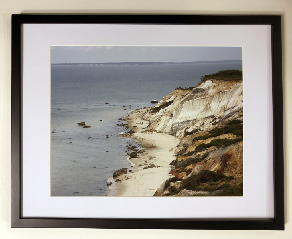 The Third Wheel, Martha’s Vineyard” (2020) by Michael Aaron Gallagher. An 11” x 14” photograph of a couple walking along the shore, while a man with a backpack stumbles along alone.